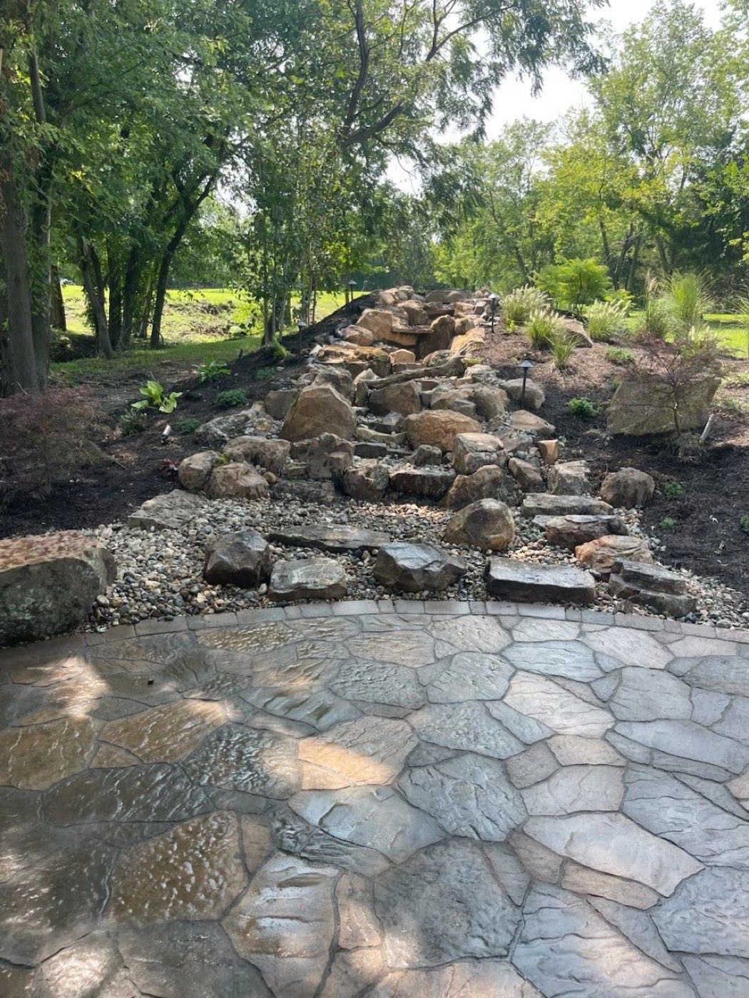 A boulder stream bed and plantings built beside a new stone patio