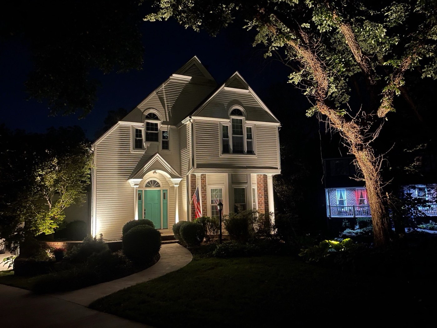 Two-story home with uplit trees and a lit walkway at night