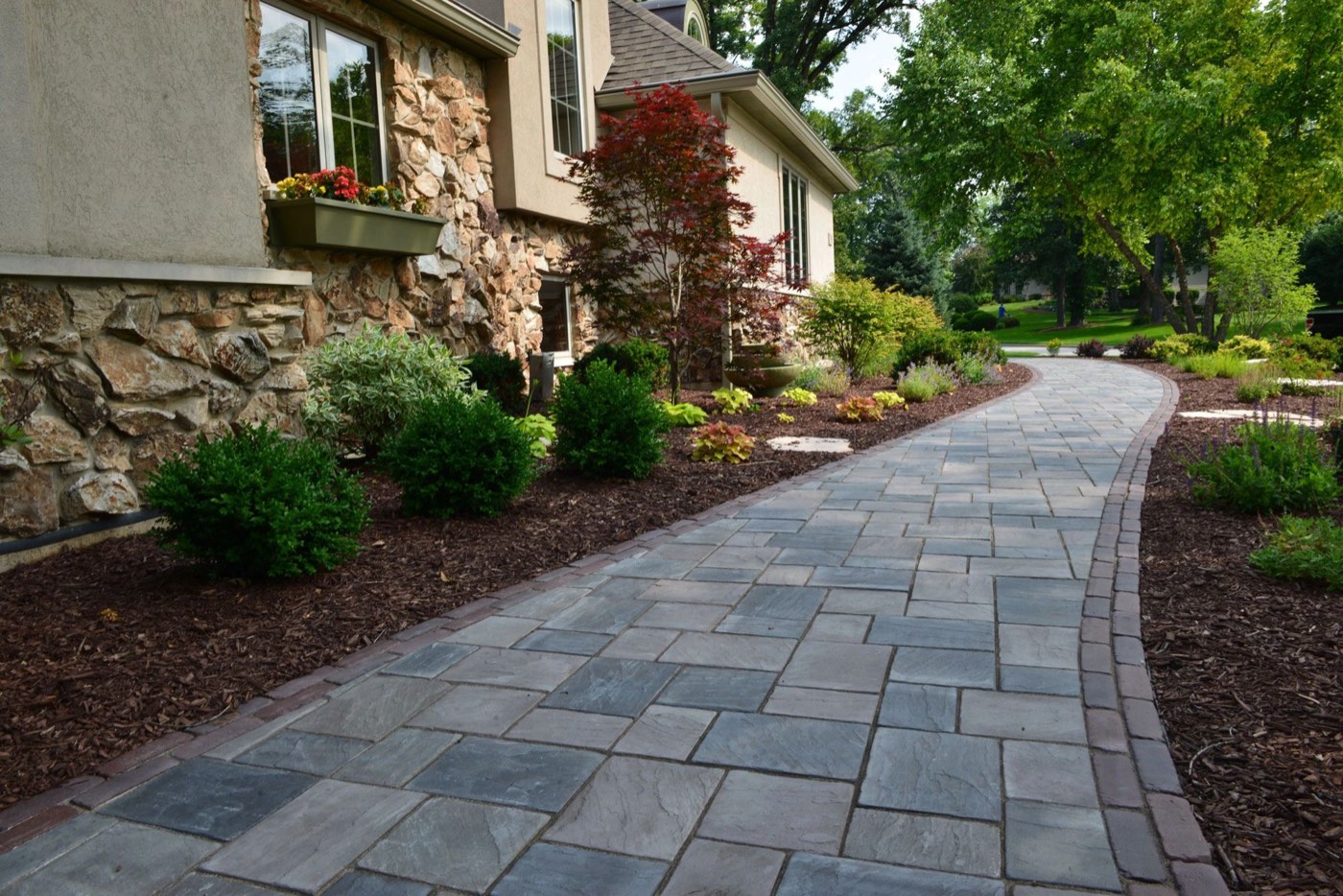 Paver walkway along a stone home between mulched beds