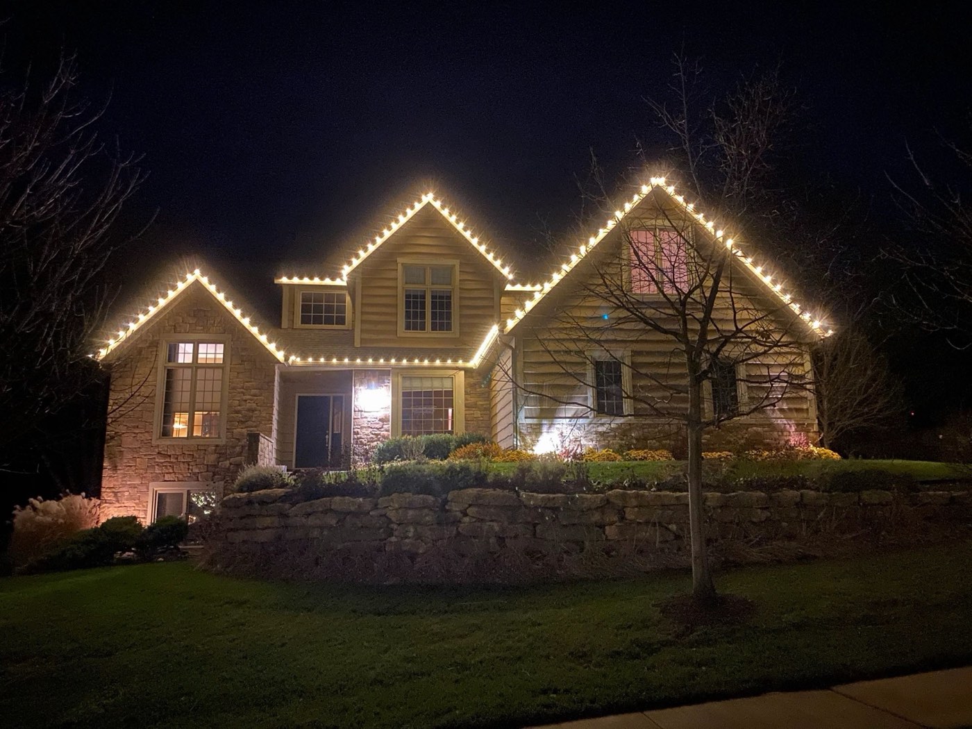 Home outlined in Christmas lights above a stone retaining wall