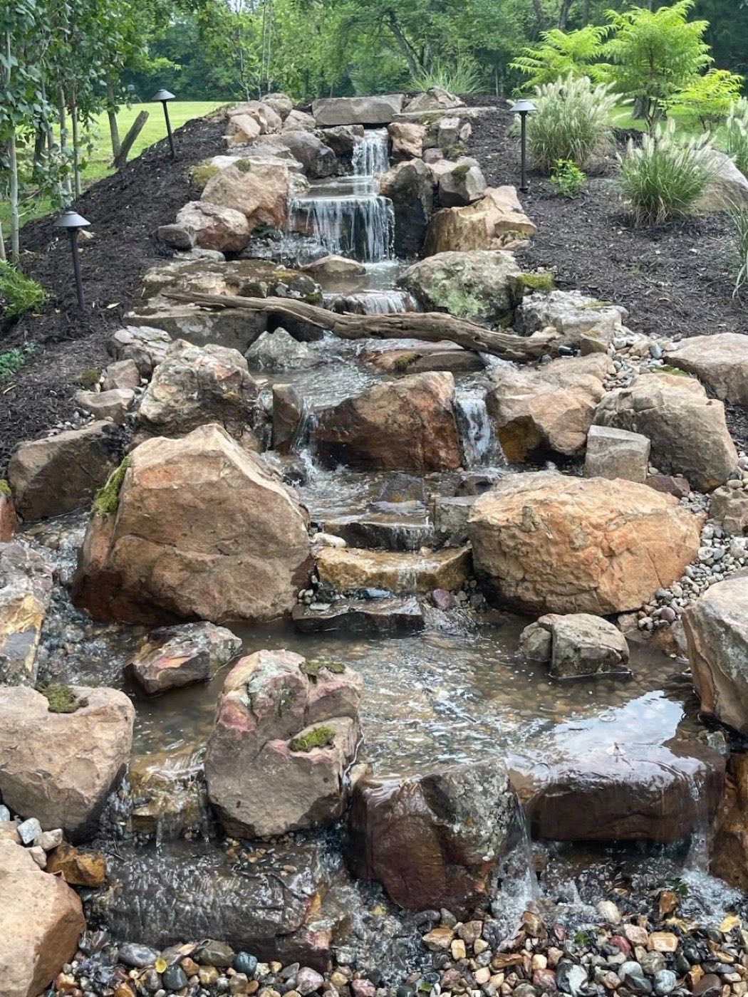 Boulder waterfall and stream flowing through a planted bed