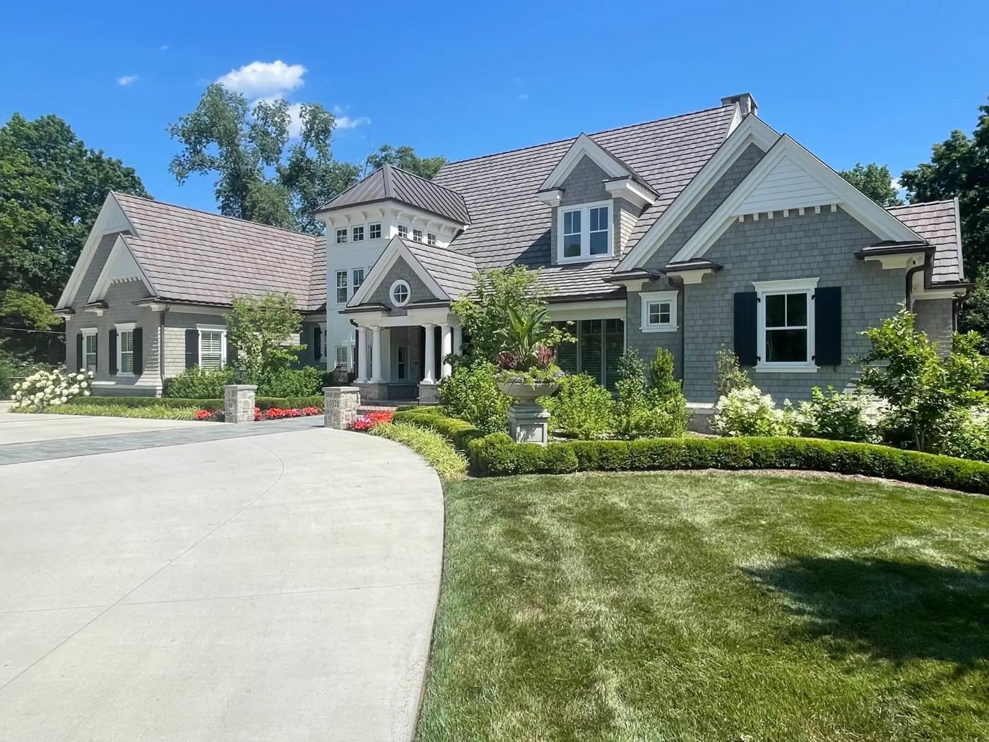 Shingle-style home with boxwood hedges, hydrangeas and a striped lawn