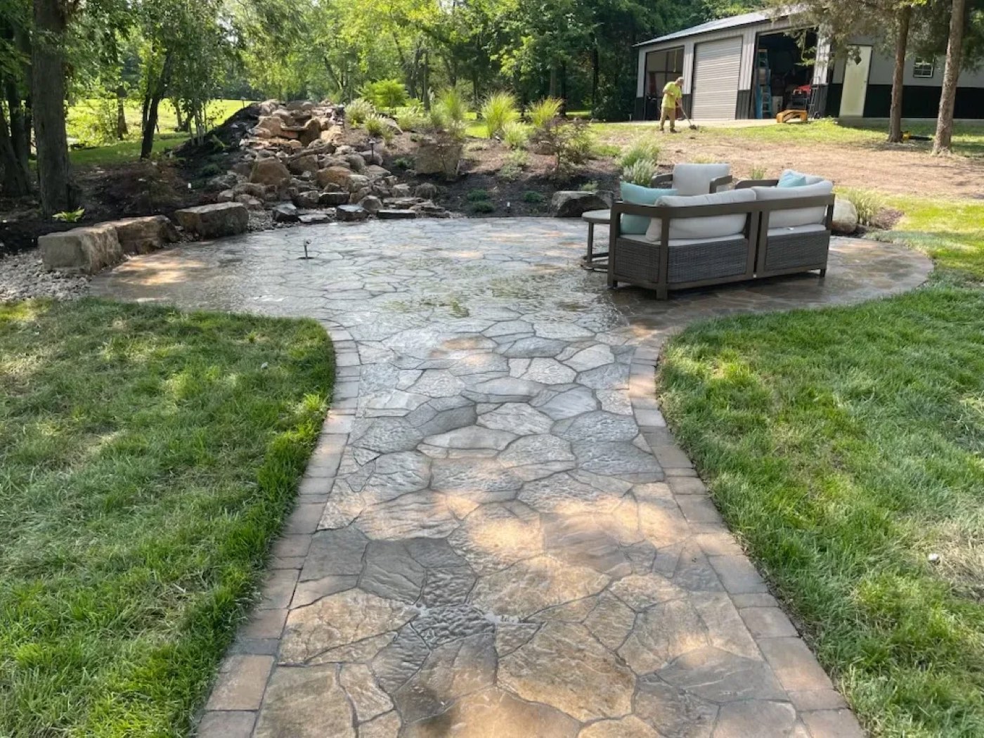 Flagstone-pattern patio and walkway in front of a boulder waterfall and new plantings